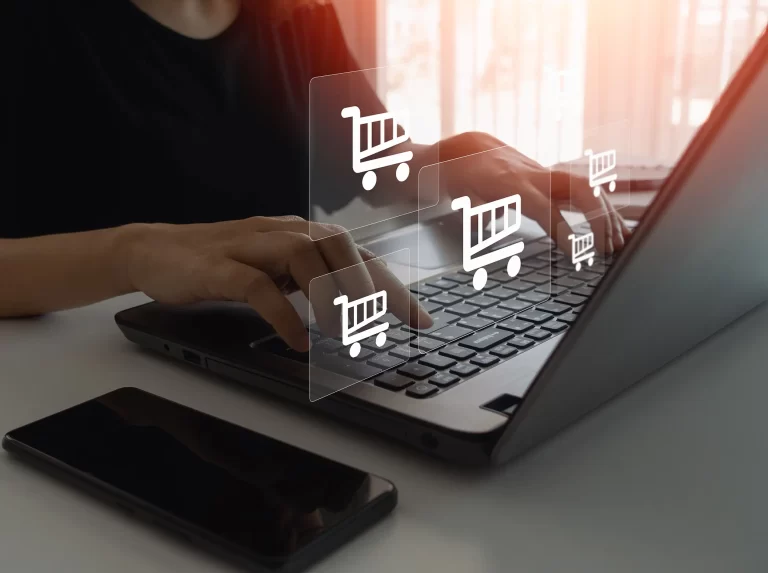 Person typing on a laptop with shopping cart icons floating, symbolizing e-commerce activity and holiday preparation.